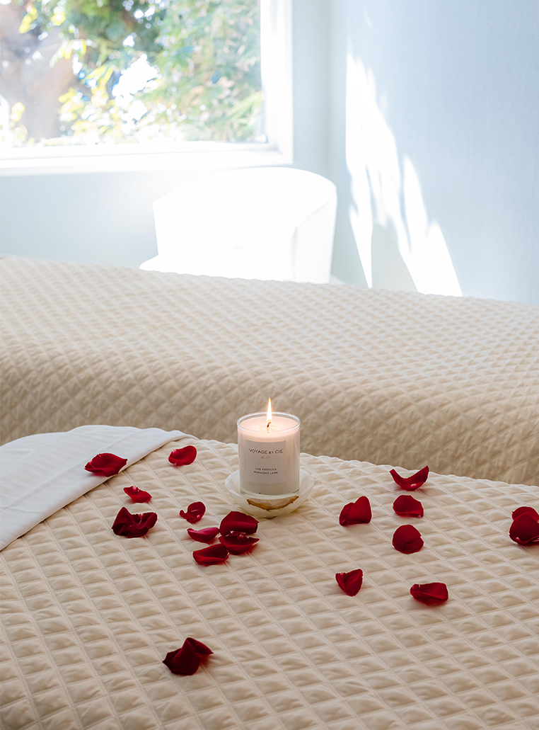 a candle and rose petals on a bed