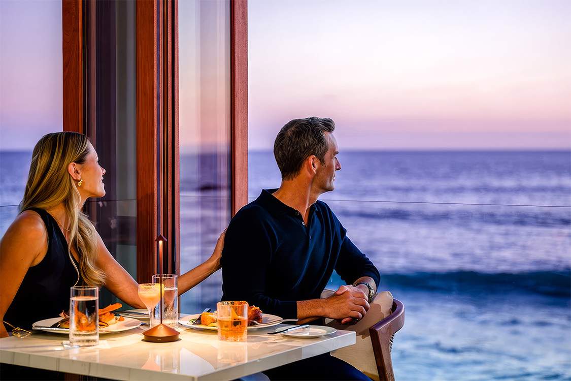 a man and woman sitting at a table with food and drinks