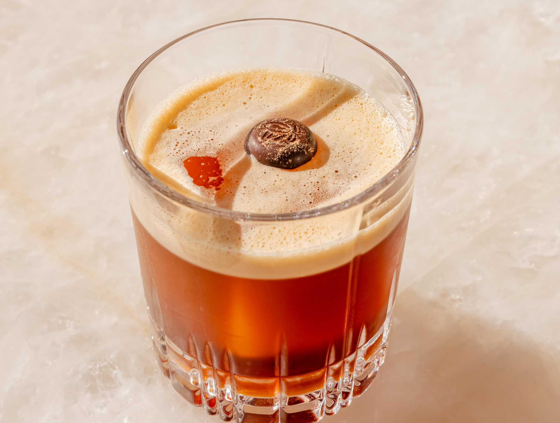 a glass of brown liquid with a round candy on top