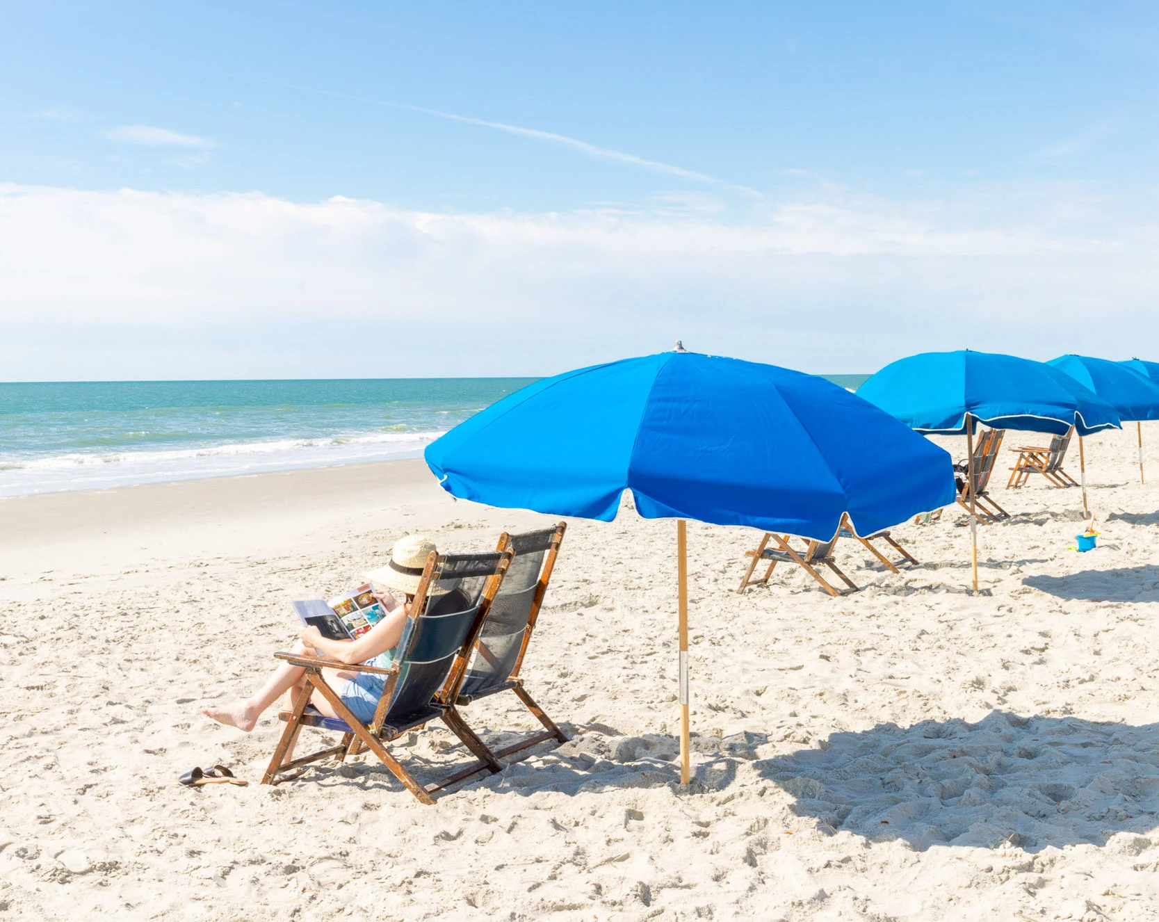 a woman sitting in a chair on a beach with blue umbrellas