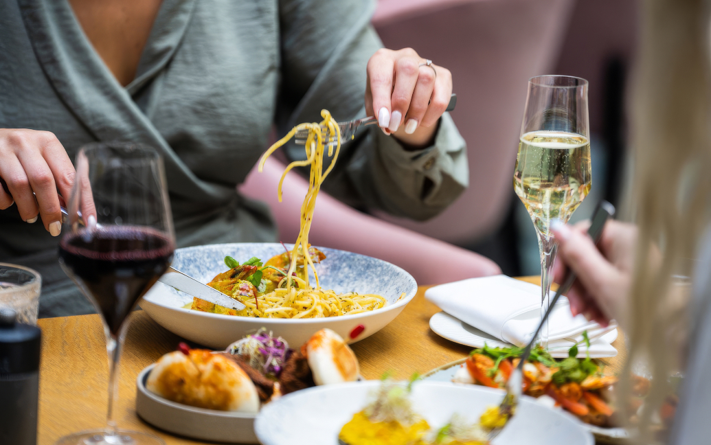 a person eating spaghetti with a glass of wine