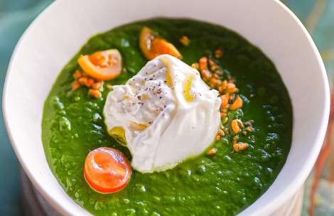 a bowl of green soup with white cream and tomatoes