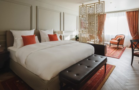 a bed with white sheets and red pillows in a room with a red chair and a red rug