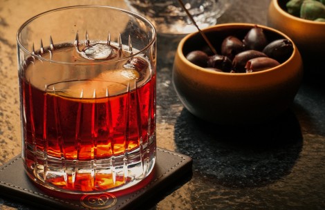 a glass of alcohol next to a bowl of olives