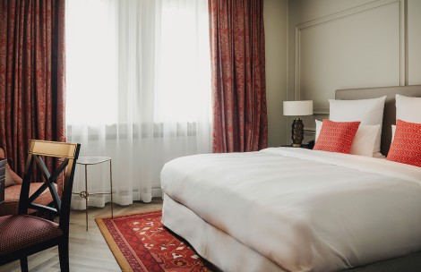a bed with a red pillow and a chair in a room with curtains