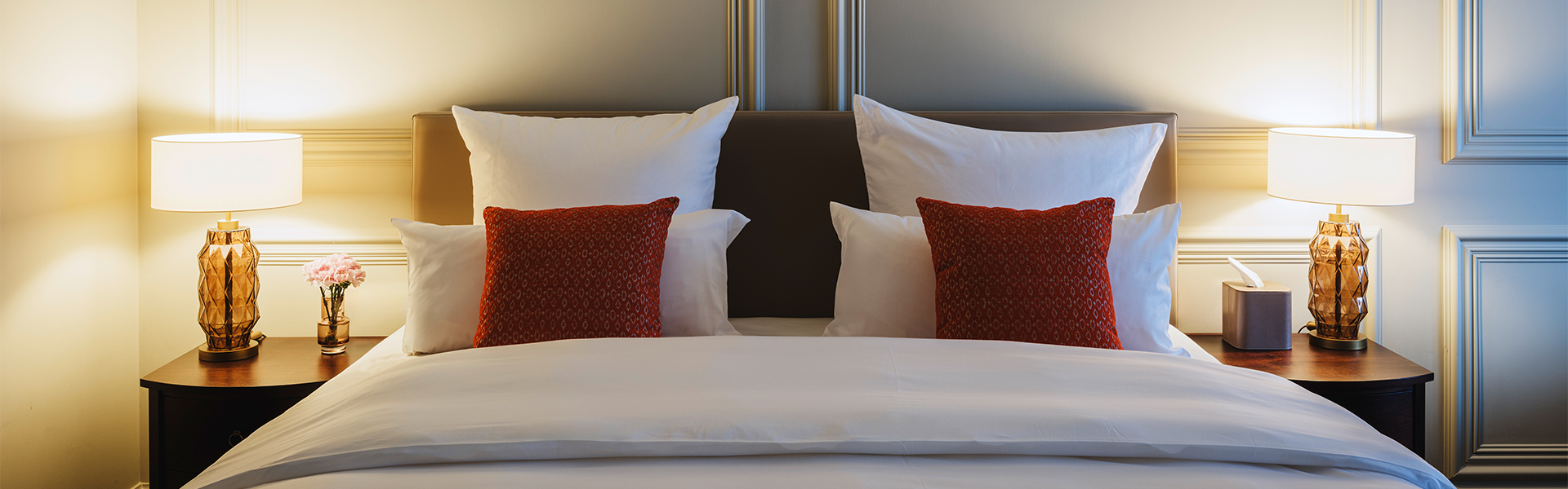 a bed with white sheets and red pillows
