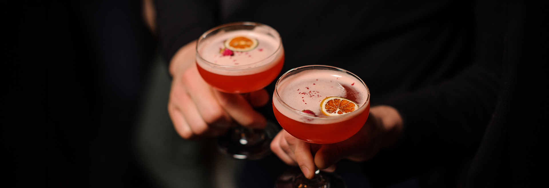 a pair of hands holding up two glasses of pink liquid