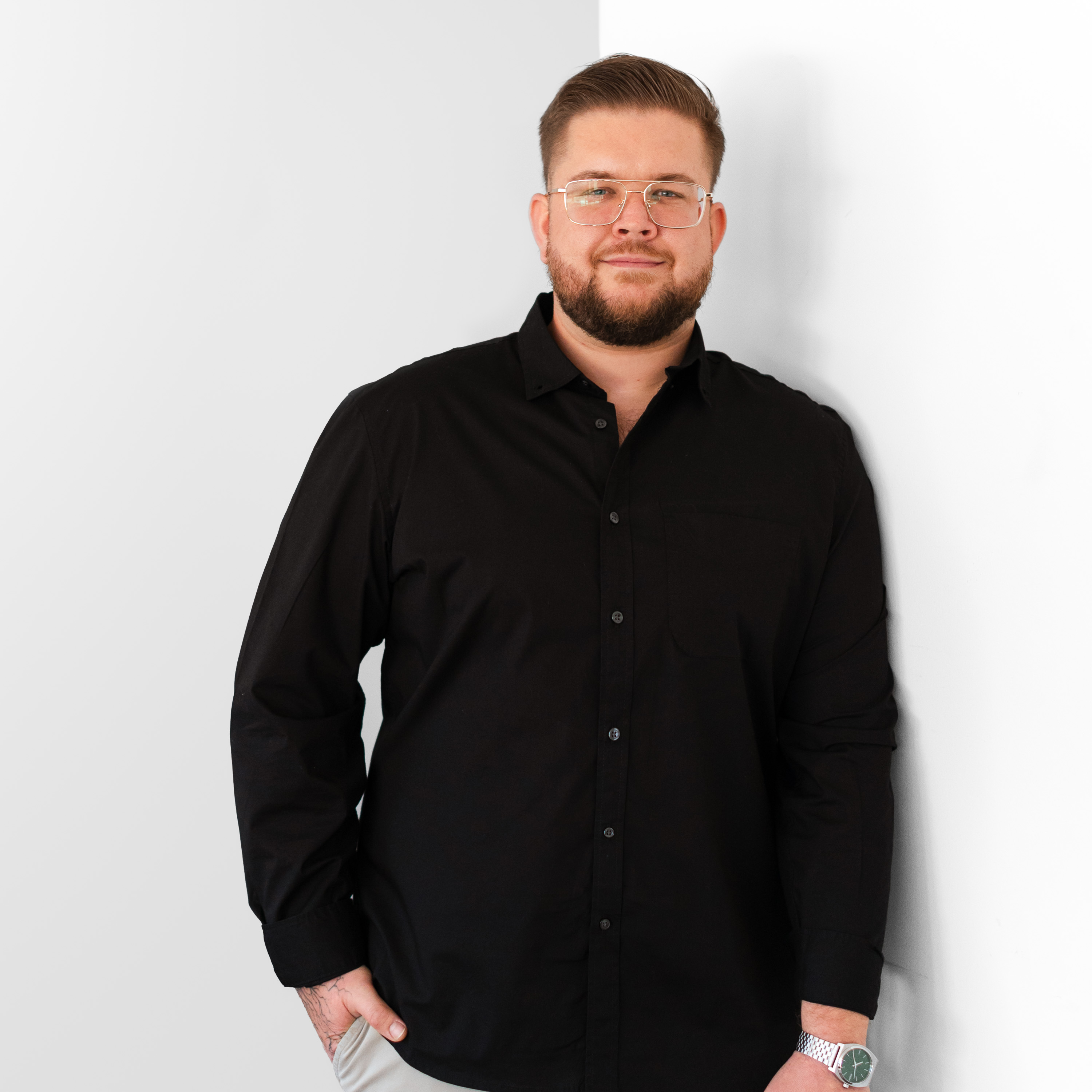 a man in black shirt and glasses leaning against a white wall