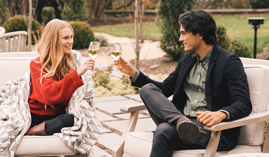 a man and woman sitting outside and holding wine glasses Preview
