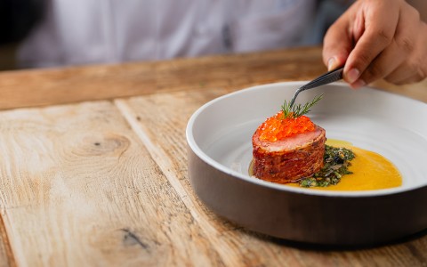 a person holding tweezers over a piece of meat with a piece of orange caviar