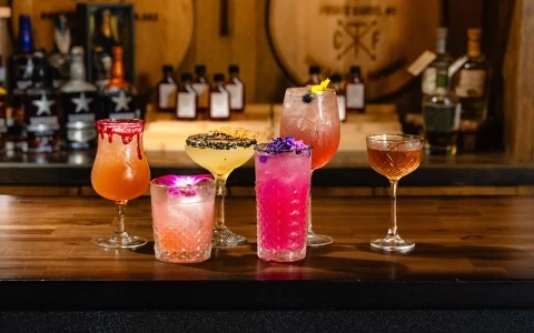 a group of different colored drinks on a bar