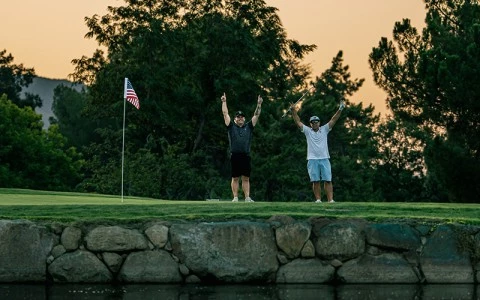 two men standing on a golf course with their arms raised