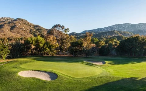 a golf course with sand bunkers and mountains in the background