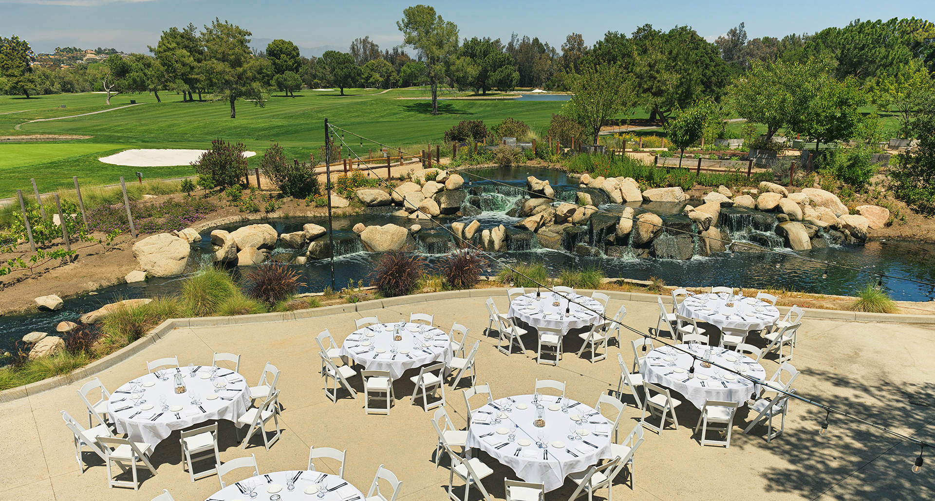 a group of tables and chairs outside with a waterfall and trees