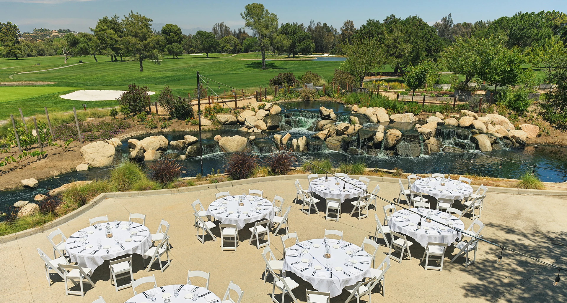 a group of tables and chairs outside with a waterfall and trees