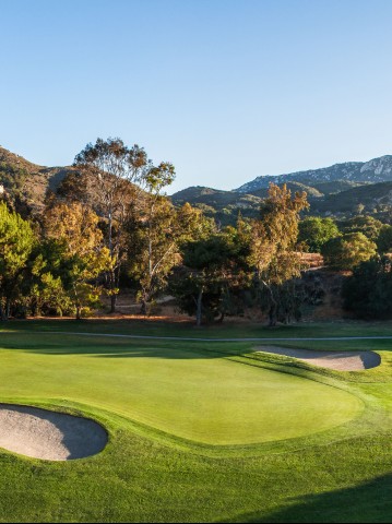 a golf course with sand bunkers and mountains in the background