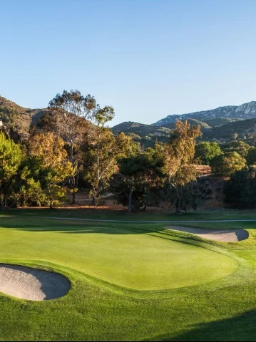 a golf course with sand bunkers and mountains in the background