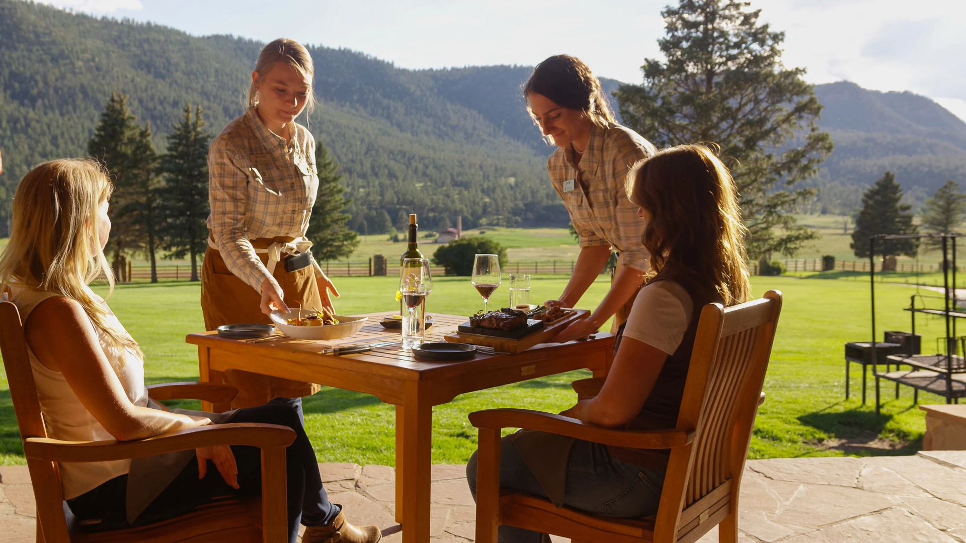 a group of women standing around a table with wine and a mountain in the background