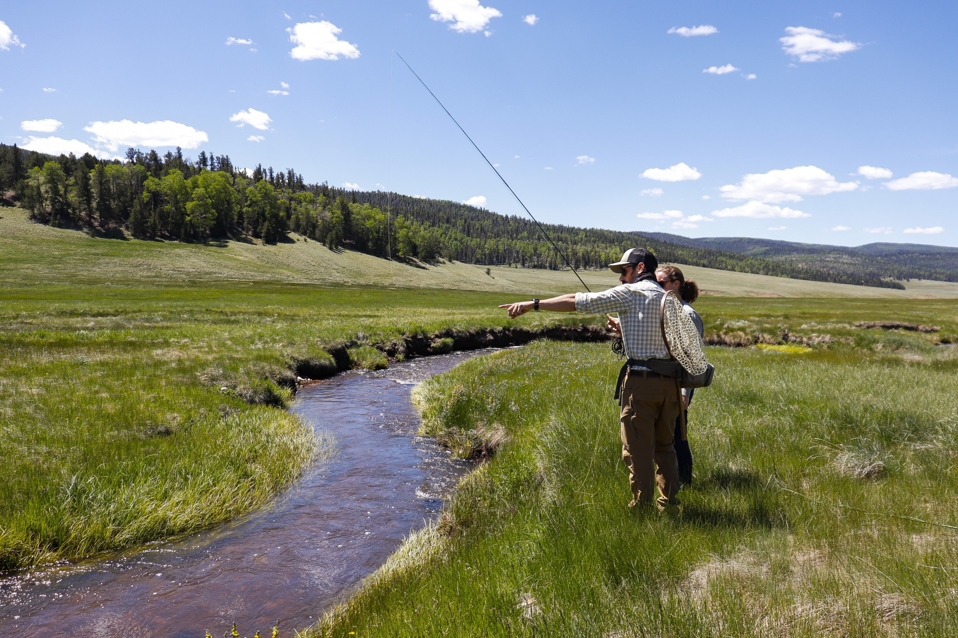 a man and woman standing in a grassy field with a fishing pole
