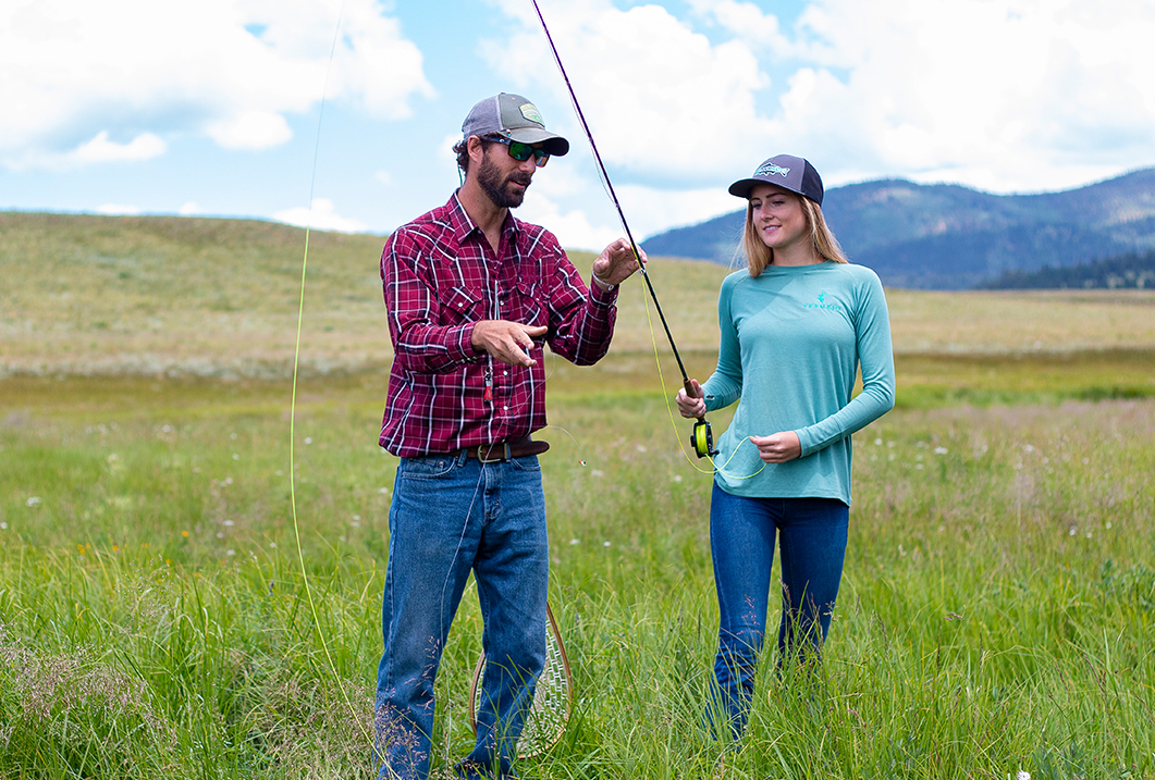 a man and woman standing in a field holding fishing rods