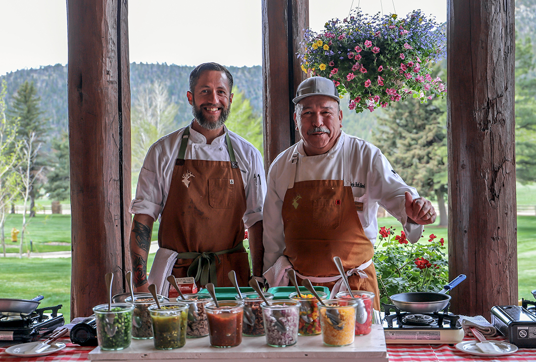two men standing in front of a table full of food
