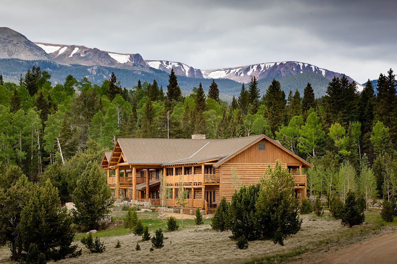 a large log cabin with trees and mountains in the background