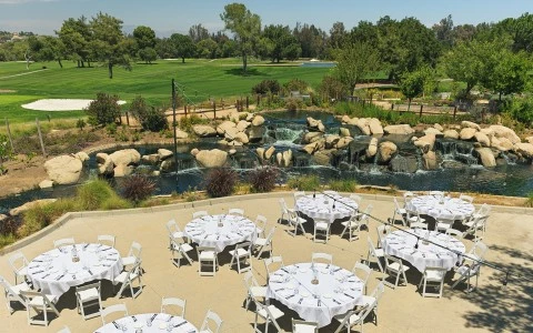 a group of tables and chairs outside with a waterfall and trees