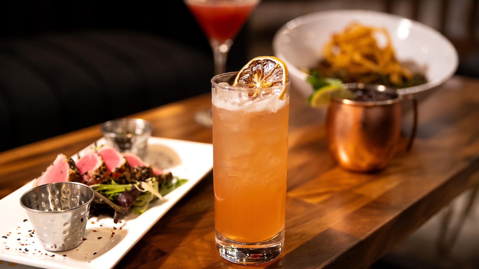 a glass of orange liquid with a slice of orange on top of a plate of food