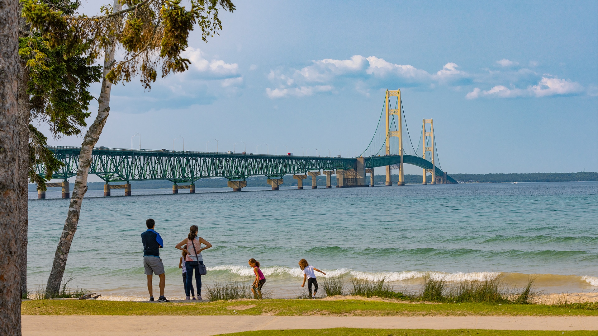 a group of people standing on a beach with a bridge in the background
