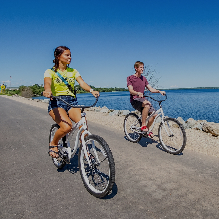 a man and woman riding bikes on a road by water
