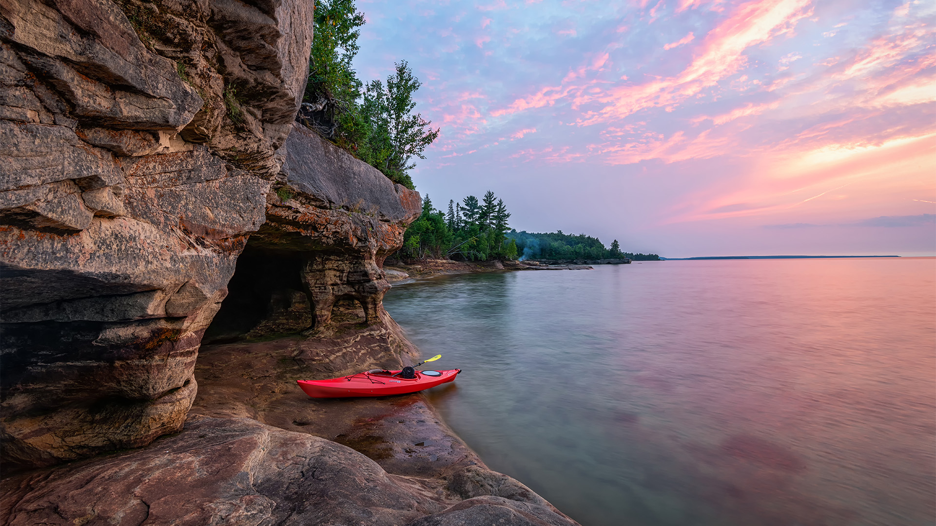 a red kayak on a rocky shore with trees and a cliff
