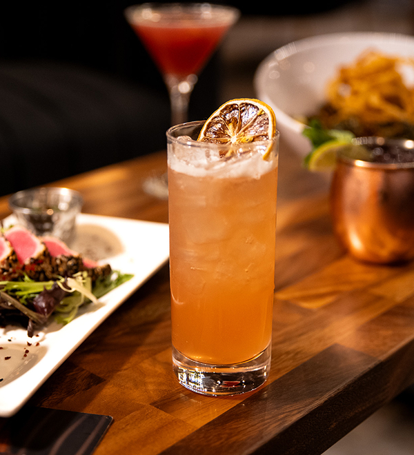 a glass of orange drink with a slice of orange on top of a plate of food