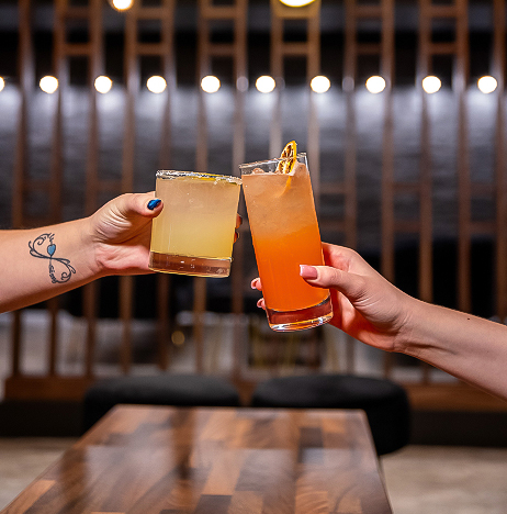a pair of hands clinking glasses with orange liquid