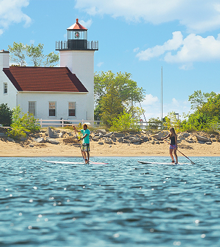 a couple of people on paddle boards in water with a lighthouse in the background