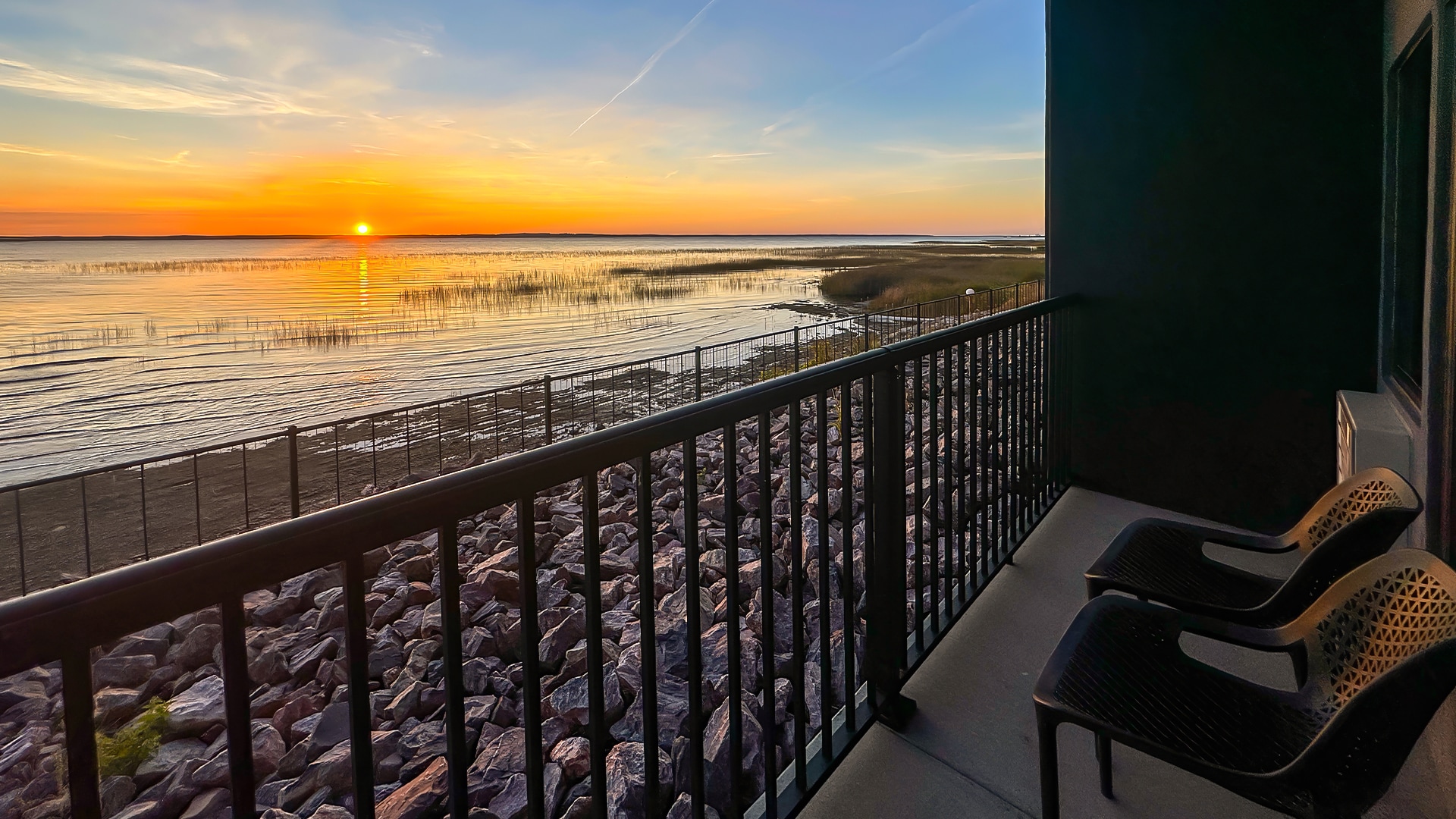 a balcony with chairs and a railing overlooking a body of water