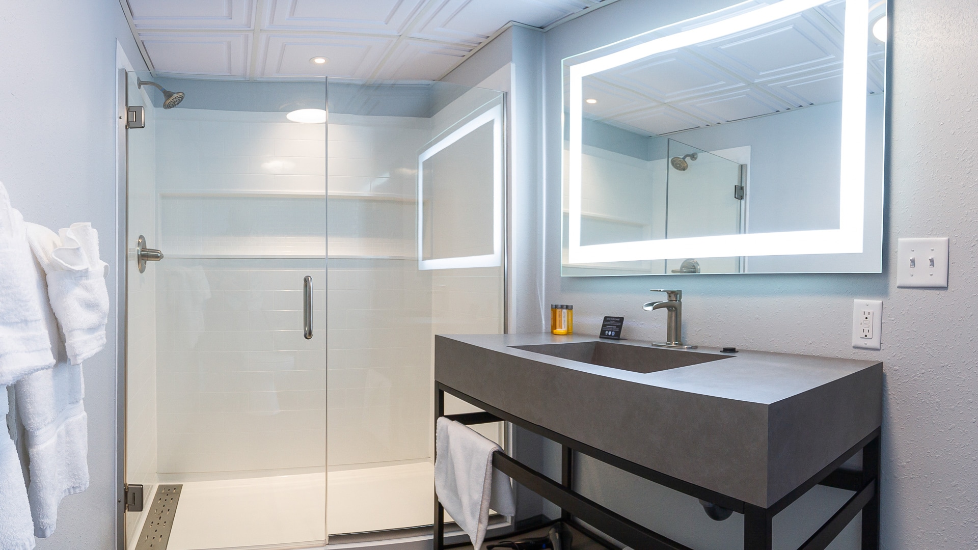 Bathroom vanity with LED mirror next to a glass shower