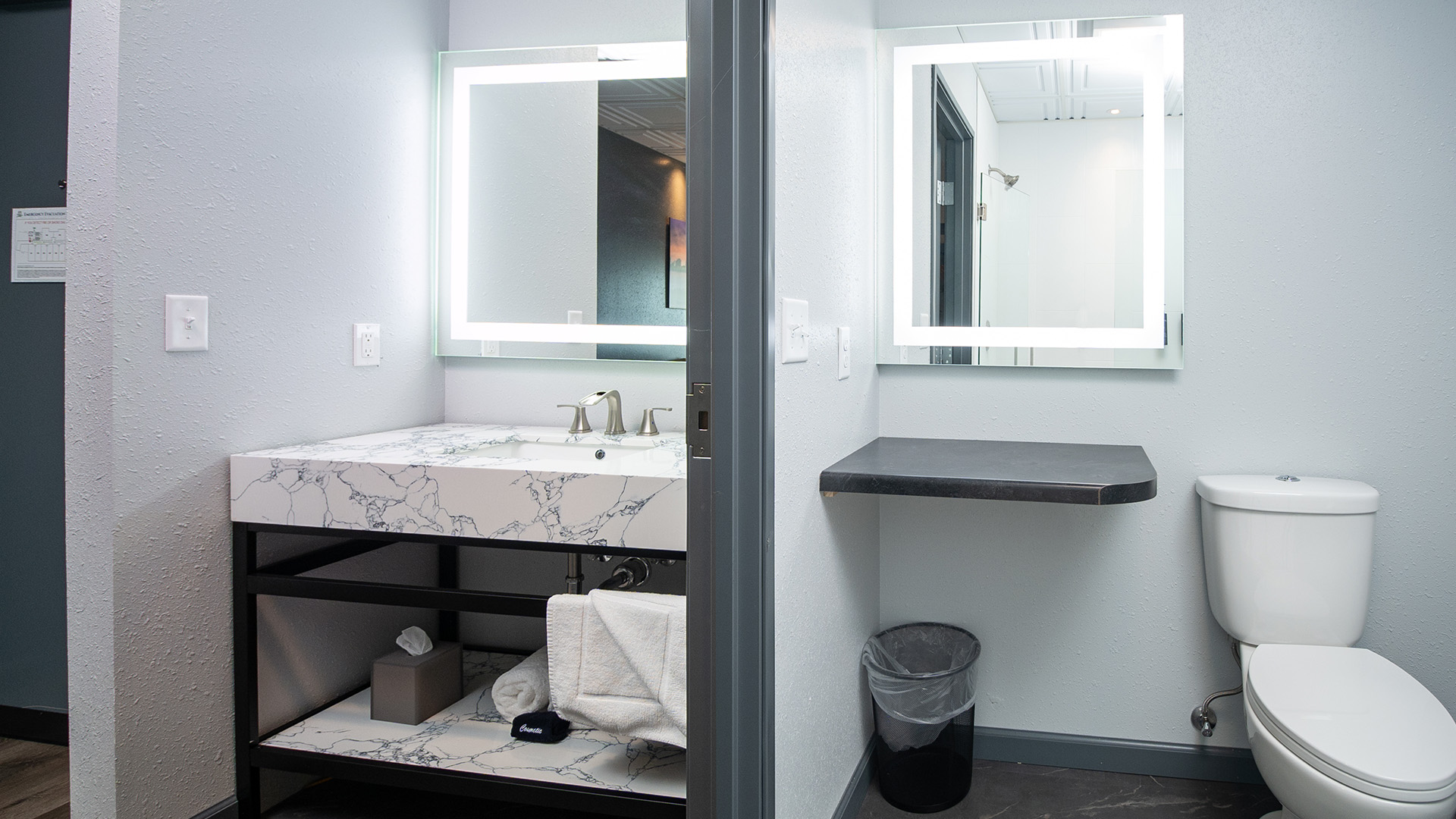 Modern bathroom with a marble vanity, toilet, and illuminated mirrors