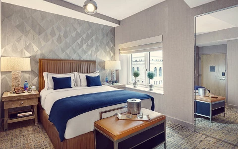 Hotel room featuring a queen bed with a nightstand on each side and a brown leather bench at the end of the bed