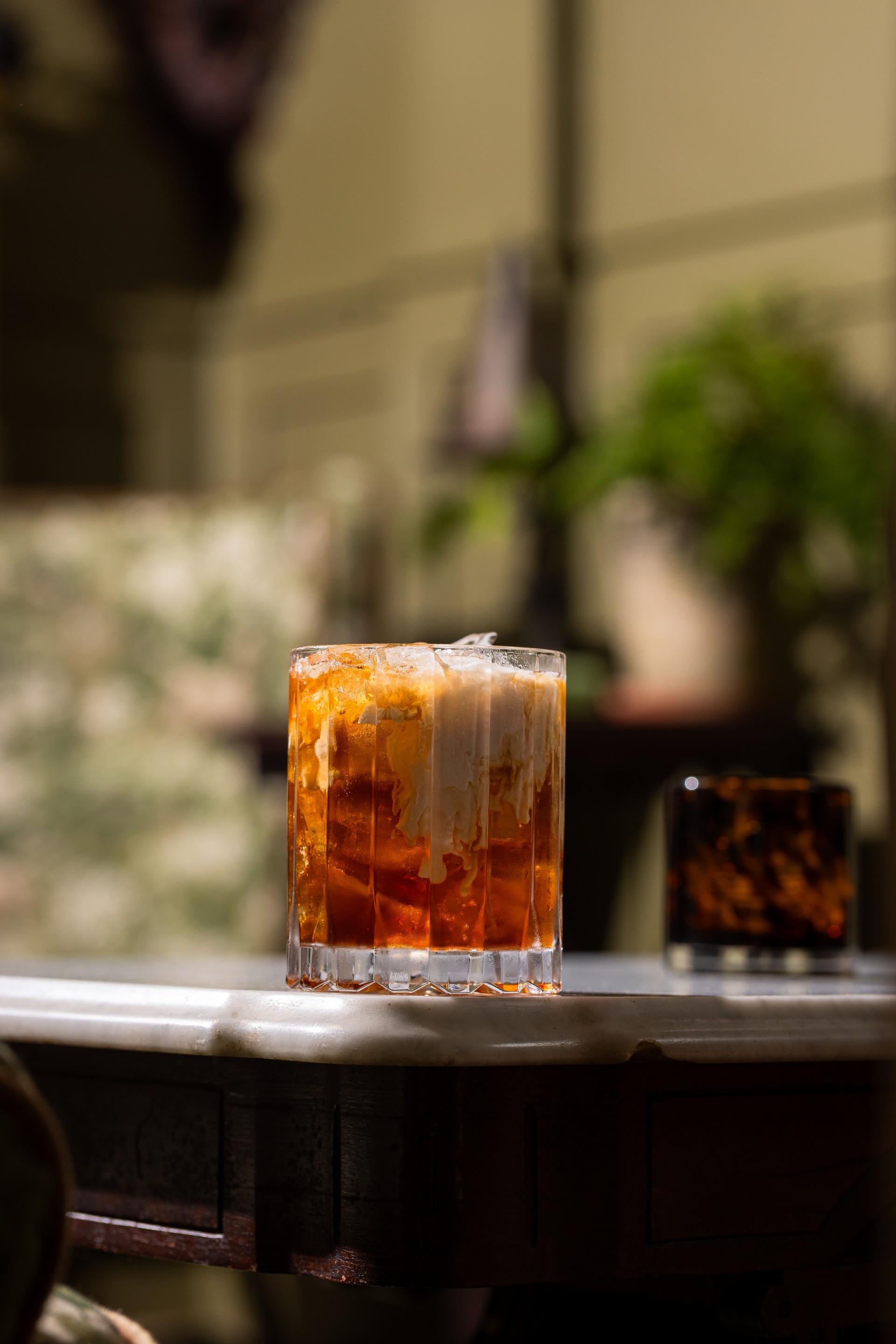 a glass with brown liquid and ice on a table