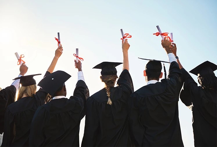 a group of people in graduation gowns and caps raising their hands up