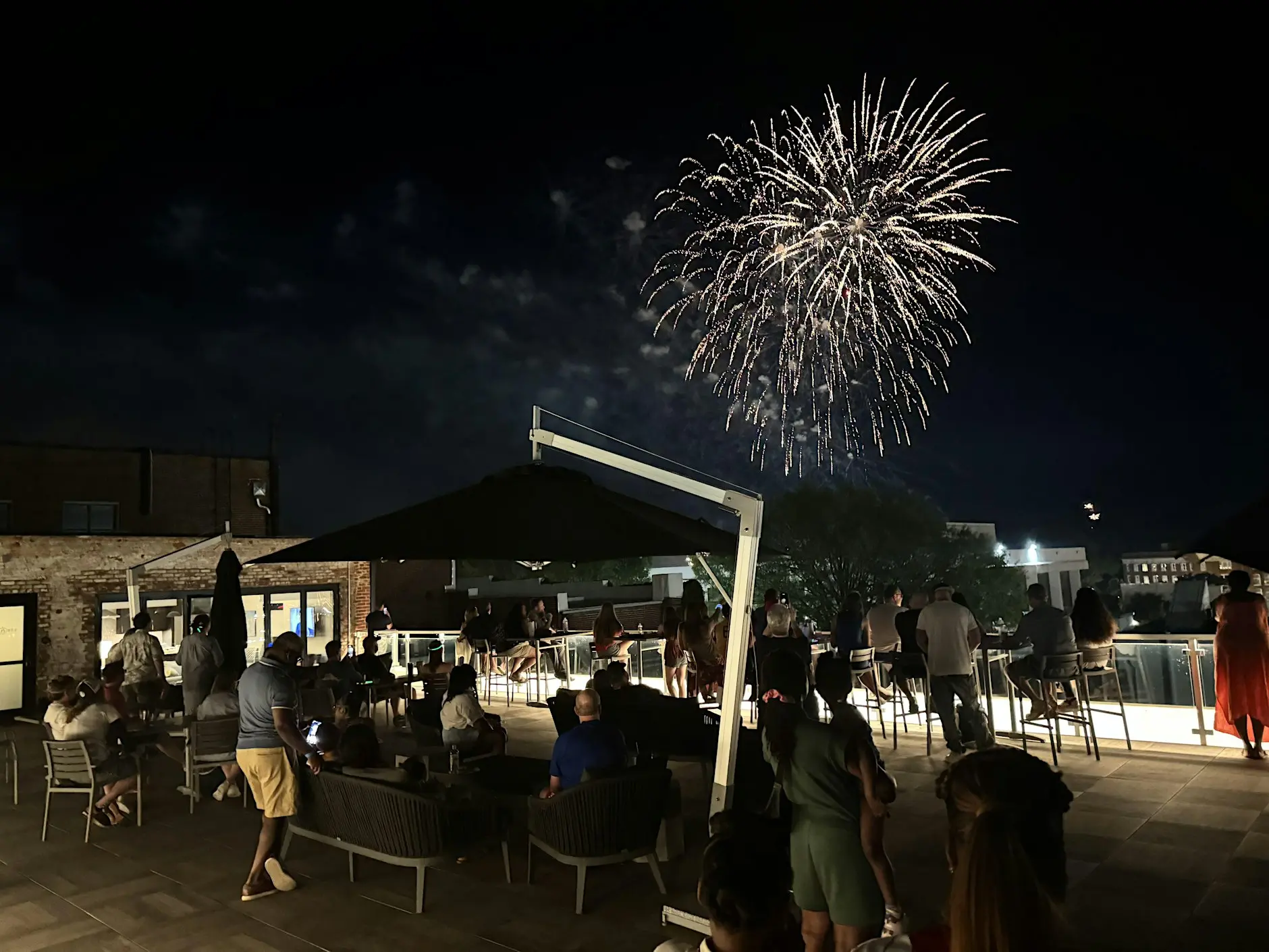 a group of people sitting around a table and chairs with fireworks in the sky