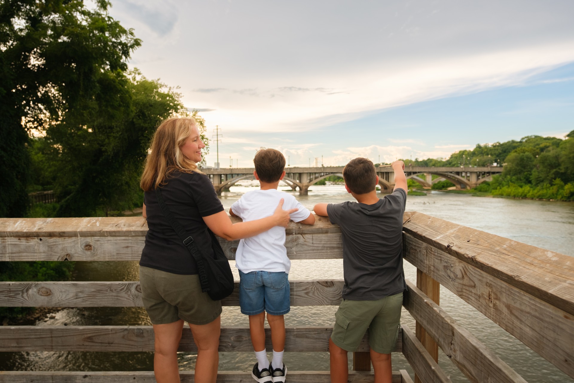 a woman and two boys standing on a wooden bridge