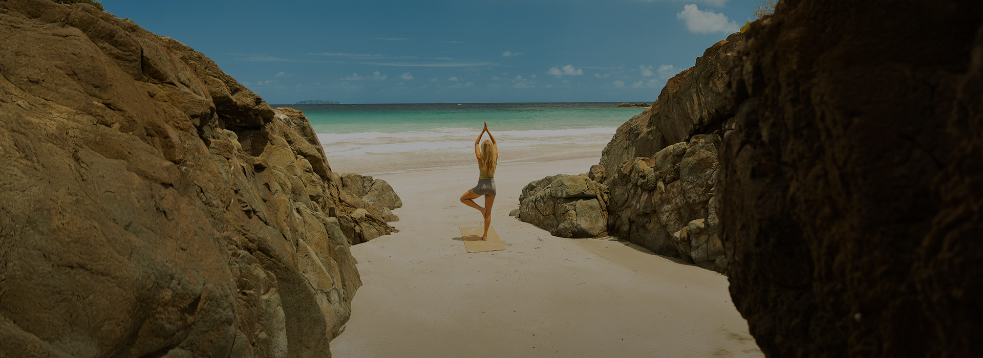 a woman standing on a yoga mat on a beach with rocks and water in the background