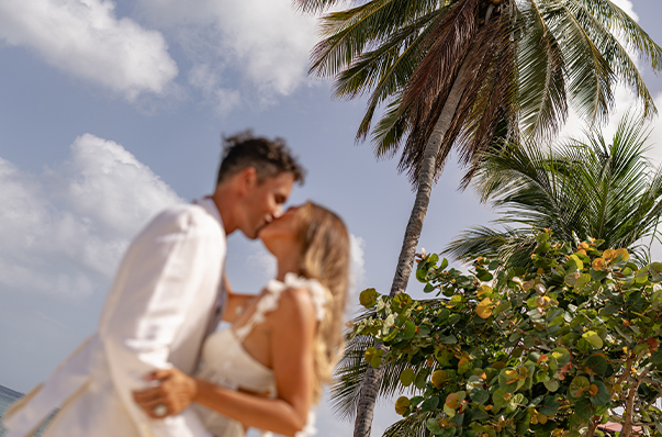 a man and woman kissing in front of a palm tree