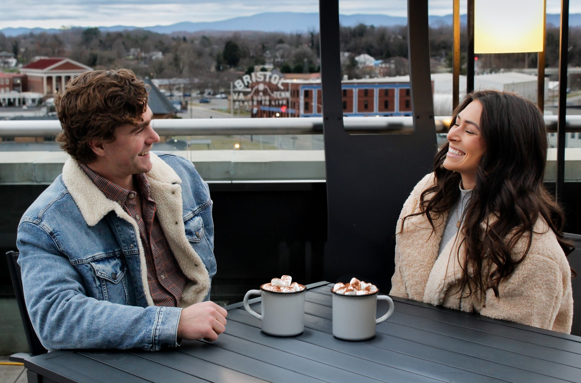 a man and woman sitting at a table with cups of hot chocolate