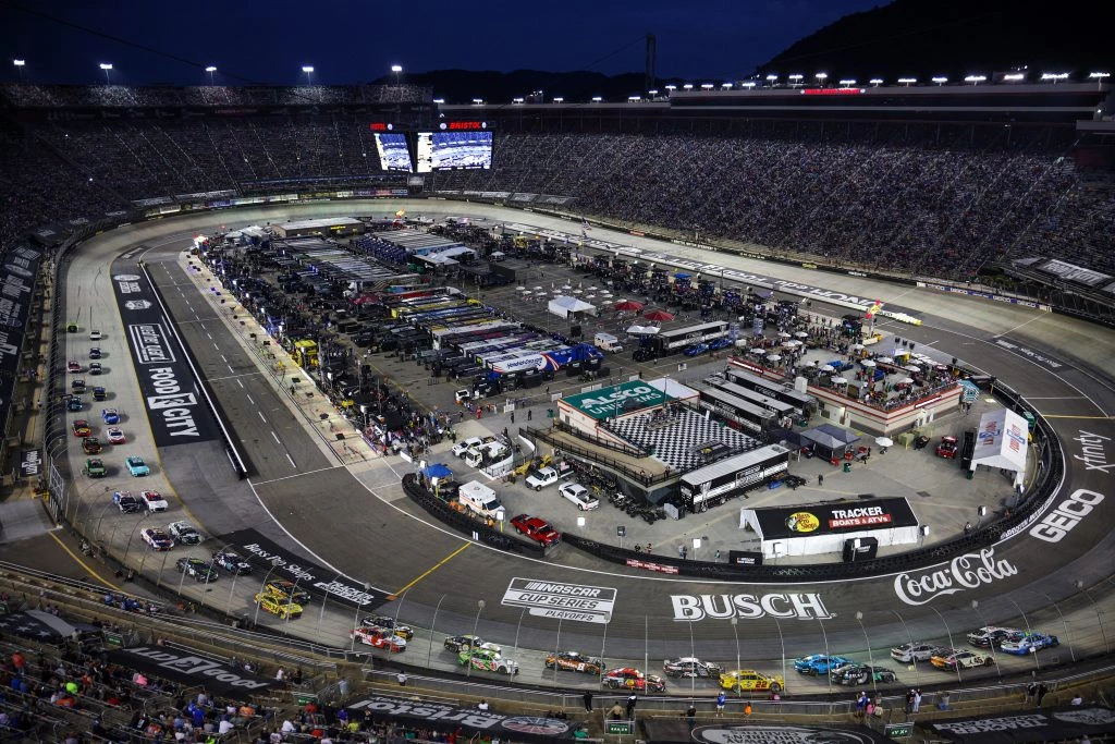 a race track with cars and people in the stands with Bristol Motor Speedway in the background