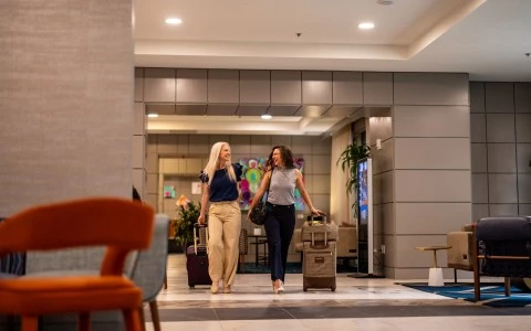 two women walking with luggage in a hotel lobby
