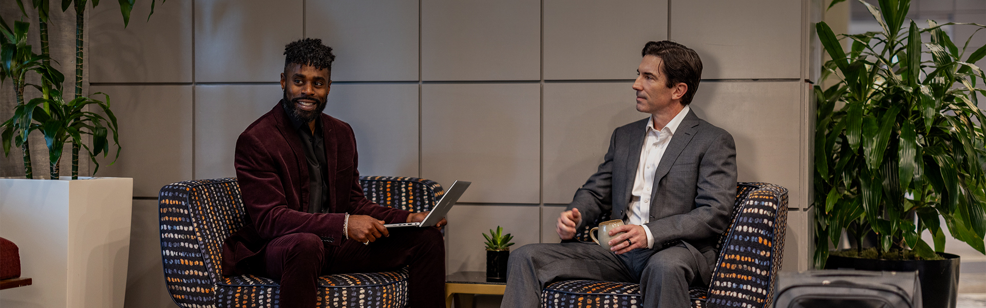 a man holding a laptop and another man sitting in chairs