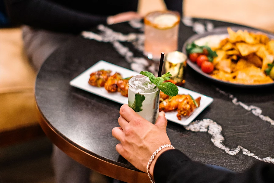 a hand holding a drink with a straw and a plate of food on a table