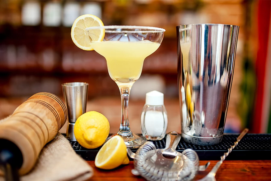 a cocktail glass with lemons and a shaker on a bar counter